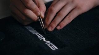 Two hands in focus while sewing the AMG lettering.